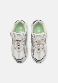 Sneakers bianchi e argento con tomaia in rete, punta rotonda e lacci beige. Presentano una soletta verde e accenti laterali testurizzati.