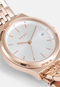 Roze-gouden metalen horloge met een ronde kast, zilveren wijzerplaat, slanke uurmarkeringen en datumweergave. Het horloge heeft een schakelen armband en sprankelende accenten.