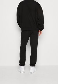 Černá oversized mikina a odpovídající kalhoty, vyrobené z měkké tkaniny. Má žebrované manžety a uvolněný střih, doplněné o bílé tenisky.