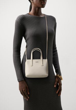 Borsa a mano in pelle beige con due manici superiori e una tracolla rimovibile, forma rettangolare, design minimalista, con logo sulla parte anteriore.