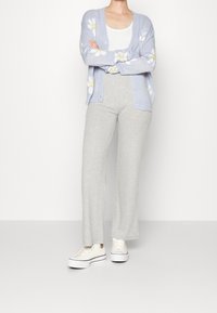 Ljusblå cardigan med gula och vita blommiga mönster, kombinerad med grå ribbade vida byxor och vita plattformssneakers.