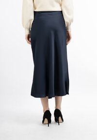 Jupe midi en satin bleu marine avec une texture lisse, un ourlet évasé et des fentes latérales, portée avec des chaussures à talons hauts noires.