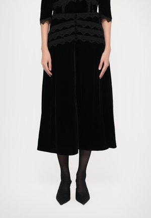 Jupe en velours noir au design fluide, ornée de détails en dentelle noire le long de la taille. Texture lisse, longueur mi-mollet.