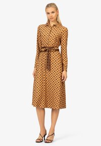 Maxikleid in Braun mit geometrischem Muster, mit Knopfleiste vorne, langen Ärmeln und passendem Taillengürtel. Glatte Textur.