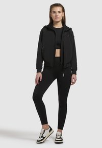 Veste bomber cropped noire, haut ajusté noir, leggings noirs et sneakers noir et blanc. Tissu texturé, fermetures éclair, design sportif.