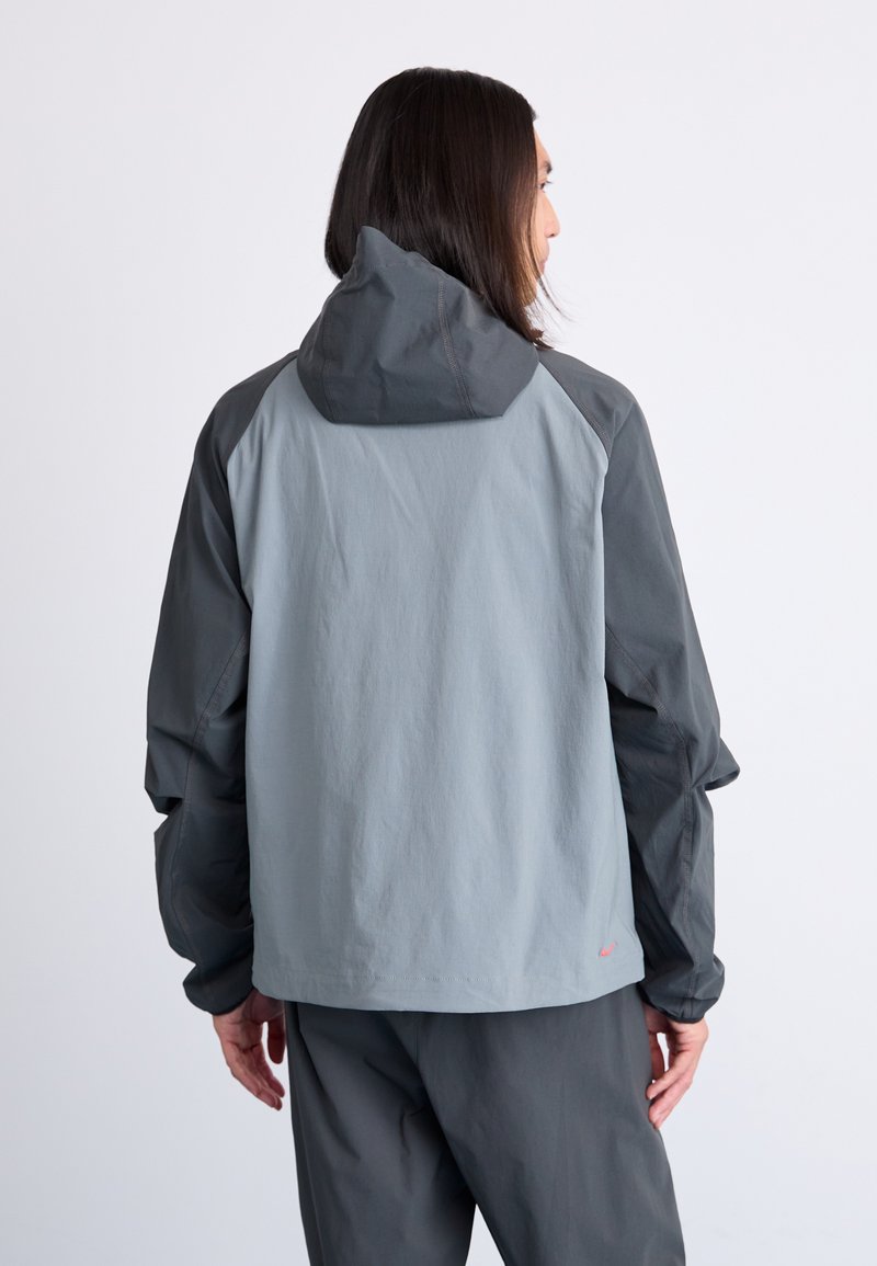 Szara kurtka z kapturem, z zestawieniem jasnoszarych i ciemnoszarych paneli. Gładka faktura, elastyczne mankiety i luźny krój.