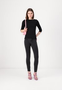 Svart tettsittende topp med trekvart erm, kombinert med svarte skinny jeans og lilla stroppesandaler. Rosa håndveske gir fargekontrast.