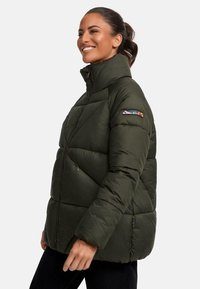 Dunkelgrüne Puffjacke mit hohem Kragen und diagonalem Nähen, ausgestattet mit Reißverschlusstaschen und einem bunten Logo am Ärmel.