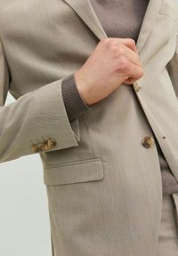 Blazer a scacchi beige realizzato in tessuto testurizzato, caratterizzato da chiusura a due bottoni, rever a punte e bottoni di accentuazione marroni.