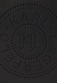 Materiale in pelle nera con un design perforato caratterizzato da fori circolari. Il motivo forma lettere e un logo al centro.