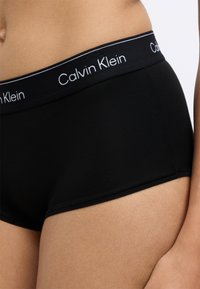 Fekete pamut boxer alsónadrág sima textúrával, fehér betűkkel ellátott márkázott derékrésszel és diszkrét varrási részletekkel.