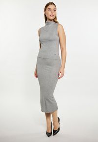 Top grigio senza maniche con collo alto abbinato a una gonna midi grigia. Texture liscia, design aderente e un sottile dettaglio del logo del brand.