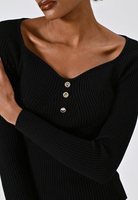 Top a costine nere con scollatura a V, caratterizzato da tre bottoni tondi e lucidi sul davanti; maniche lunghe; tessuto testurizzato.