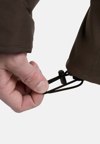 Braune Jacke mit verstellbarem Ärmel, ausgestattet mit einem schwarzen Kordelzug und Zugband. Nahaufnahme einer Hand, die den Zugmechanismus hält.