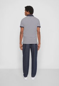 Stripet polo skjorte i navy og hvid, kortærmet med mørke manchetter, parret med mørke denimbukser og hvide sneakers.