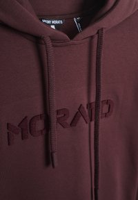 Felpa bordeaux con tasca a marsupio frontale, caratterizzata da un logo "Morato" ricamato. Realizzata in tessuto morbido con dettagli in cordino testurizzati.