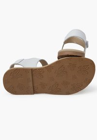 Sandale en cuir blanc avec deux sangles et une semelle en caoutchouc marron, ornée de motifs de papillons en relief. Le design est ouvert au niveau des orteils.