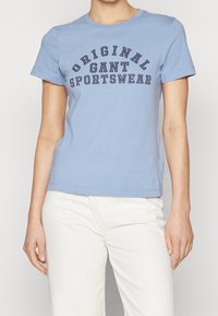 T-shirt di cotone blu chiaro con maniche corte, scollatura rotonda e scritta scura che recita "ORIGINAL GANT SPORTSWEAR" sul davanti.