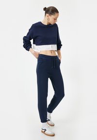 Marineblauwe cropped sweatshirt met lange mouwen over een witte ondershirt, gecombineerd met marineblauwe joggers met zijzakken en elastische boorden.