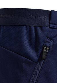 Nahaufnahme von marineblauen Sporthosen mit elastischem Bund, geprägt mit Markenlogo, und einer seitlichen Reißverschlusstasche.