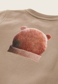 Felpa beige con un motivo stampato di un cappello di lana marrone con due piccole orecchie a pompom sul retro.
