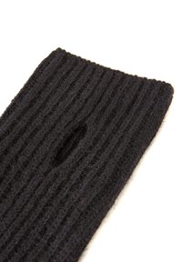 Tela de lana negra acanalada con forma rectangular y un pequeño corte ovalado en el centro, que muestra una superficie texturizada.