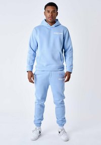 Sudadera y pantalones jogger de color azul claro, hechos de una tela suave, con un bolsillo canguro central y un pequeño logotipo de texto blanco en el pecho y el muslo.