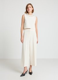 Haut court sans manches blanc à texture côtelée, orné d'un col perlé, associé à un pantalon large crème et des talons pointus noirs.