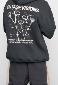 Czarny, oversize'owy hoodie z białym nadrukiem graficznym przedstawiającym kwiaty oraz tekst na plecach. Materiał wydaje się miękki, z detalami w ribb. 