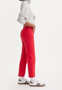 Jeans rojos de cintura alta en denim, corte recto, con dos bolsillos traseros. Combinados con una sudadera gris de manga larga y zapatillas blancas.