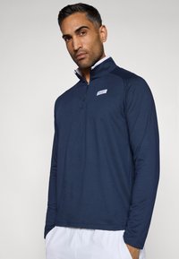 Pullover de mangas compridas azul-marinho com zíper de um quarto, tecido leve, com detalhes em branco no colarinho e um pequeno logotipo no peito.