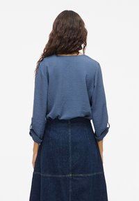 Blaue strukturierte Bluse mit Dreiviertelärmeln, kombiniert mit einem dunklen Jeansrock mit sichtbaren Nähten und einem ausgestellten Schnitt.