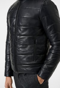 Schwarze Lederjacke mit gestepptem Design, Reißverschluss vorne und Seitentasche. Sie zeichnet sich durch eine glatte Textur und eine taillierte Silhouette aus.