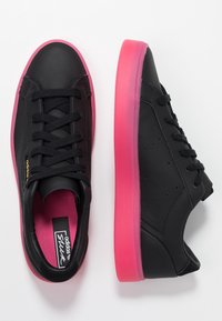 Black leather sneakers with pink translucent sole, featuring lace-up design and perforations on sides for ventilation. Accented with logo.