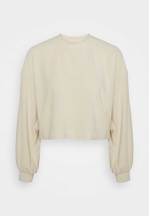Zkrácený top s dlouhým rukávem v světle béžové barvě s texturovaným vaflovým vzorem a elastickými manžetami. Kulatý výstřih a volnější střih.