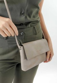 Lys grå læder crossover taske med klaplukning, let struktureret overflade og en tynd rem. Kompakt design velegnet til det vigtigste.