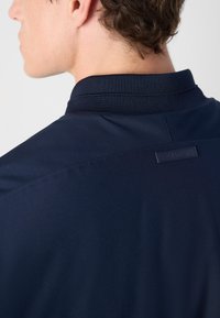 Polo shirt bleu marine avec un col texturé, comportant une petite étiquette de marque à l'arrière. Tissu lisse avec une coupe ajustée.