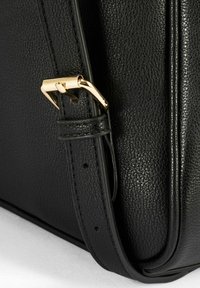 Czarna skórzana torebka z fakturowaną powierzchnią, złotym metalowym zapięciem i usztywnionym kształtem z akcentującym przeszyciem.
