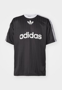 Musta urheilupaita, joka on valmistettu sileästä kankaasta, ja jossa on valkoinen "adidas"-logo sekä kolme valkoista raitaa hihoissa. Pyöreä kaula-aukko.