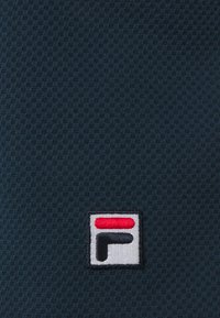 Námořnická tkanina s texturou obsahuje čtvercové logo s červenou vodorovnou čárou a bílým obrysem, umístěným blízko dolního rohu.