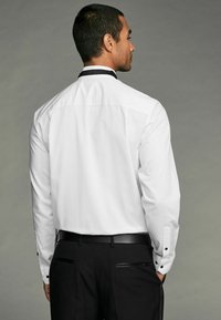 Cămașă albă cu mâneci lungi, guler negru, manșete cu nasturi și un finisaj de țesătură netedă. Purtați cu pantaloni negri.
