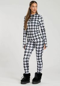 Body in stampa houndstooth bianco e nero con colletto con zip; design aderente. Gli accessori includono calzature con fodera in pelliccia nera.