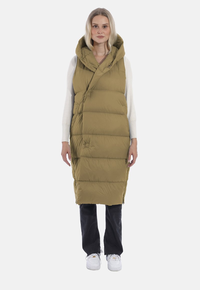 Olivgrüne, gepolsterte Weste mit Kapuze, die einen diagonalen Frontverschluss und ein knielanges Design aufweist. Kombiniert mit dunklen Jeans und weißen Sneakers.