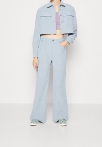 Ljusblå kordjacka i croppad modell med två bröstfickor, parat med matchande högmidjade utsvängda byxor och rutig sneakers.