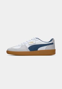 Baskets basses Puma Palermo en blanc et gris avec une bande en daim bleue et une semelle en caoutchouc marron, vues de profil.