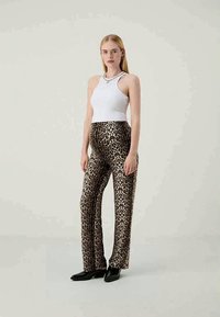 Παντελόνι με σχέδιο λεοπάρ φτιαγμένο από μαλακ�ό ύφασμα, σε συνδυασμό με μια εφαρμοστή λευκή φανέλα. Το μοντέλο φοράει μαύρα παπούτσια, με ομαλή υφή και κλασικό σχήμα.