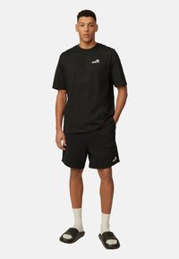 Czarna bawełniana koszulka z logo na piersi, w połączeniu z czarnymi szortami i sandałami wsuwanymi, uzupełniona białymi skarpetkami do kostek.