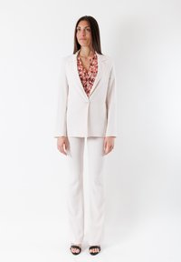 Completo beige chiaro con giacca su misura e pantaloni aderenti, con una blusa floreale underneath. Tessuto morbido e design semplice.