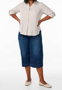 Camicia a righe beige chiaro con maniche arrotolate; abbinata a culotte in denim blu scuro e ballerine beige. Design semplice e casual.