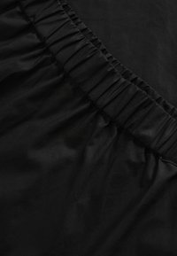 Tela negra con una textura suave, que presenta una cintura elástica con fruncido. El diseño general es simple y minimalista, enfatizando el material.